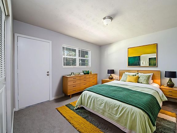 Bright modern bedroom featuring a cozy double bed with green and yellow accents, elegant wooden furniture, and vibrant wall art.