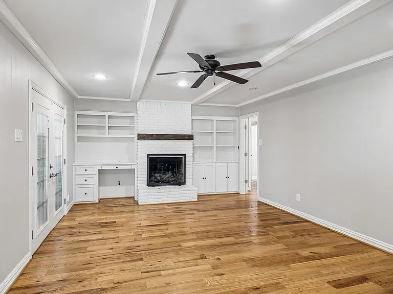 Living area featuring wood-finish flooring, a white brick fireplace with a wood mantle, and built-in shelving with a desk