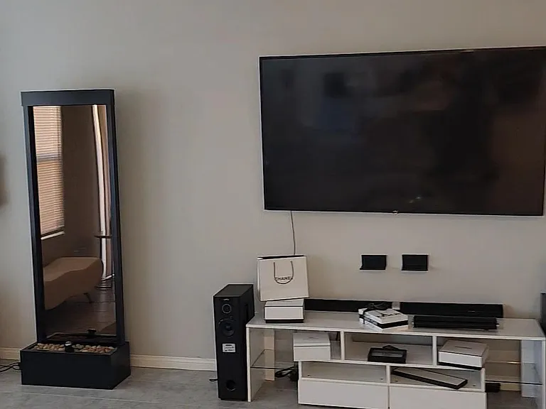 Open living area with tile floors, ceiling fan, and media setup with wall-mounted TV and console for shared lounging.