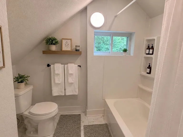 Clean full bath with tub/shower combo, built-in shower shelving, and a window for natural light and ventilation.