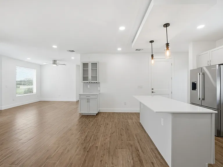 Bright open-concept living with abundant natural light. Modern kitchen features a large island, quartz countertops, and stainless steel appliances. A floating ceiling with integrated lighting above the island adds a warm, inviting ambiance.