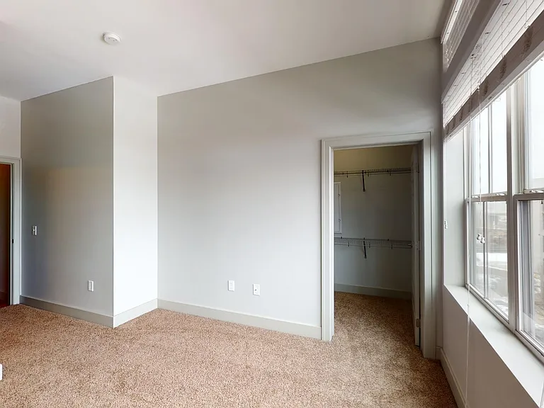 Spacious apartment bedroom with large closet, attached bathroom, and plush carpet flooring.