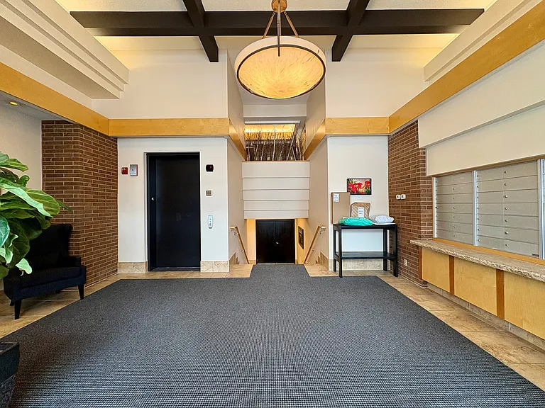 Main entrance lobby with mail box, delivery pickup table, elevator and stairs to lower garage beyond.