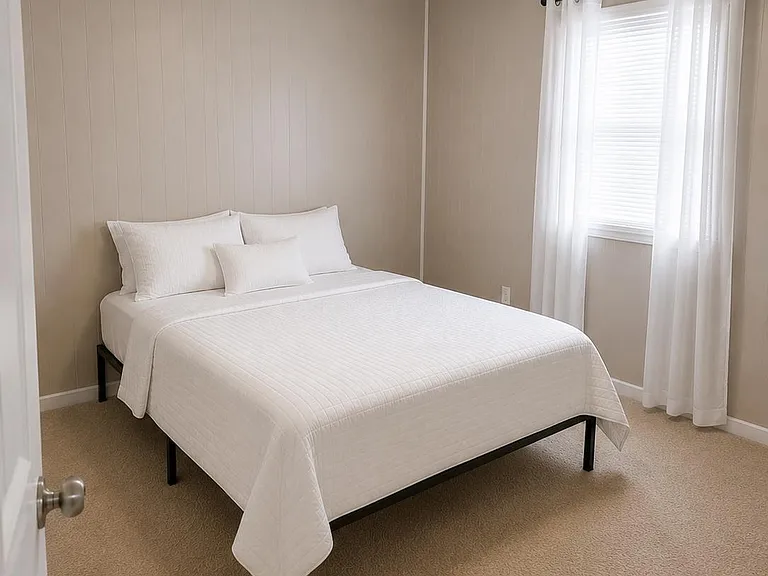 Comfortable bedroom with a full-size bed, plush carpeting, and a window dressed with curtains and blinds for privacy.