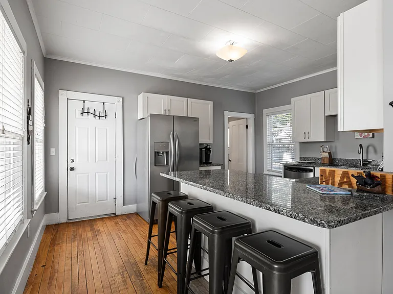 The kitchen features sleek, granite countertops on a large island that comfortably seats four on modern, black counter stoolsperfect for breakfast, casual meals, or remote work. You'll find bright, white cabinetry and stainless steel appliances, including