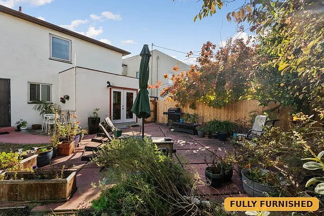 Back of the house showing the glass double doors to the bonus space/laundry, as well as showing the backyard patio where the BBQ and sun loungers are located.