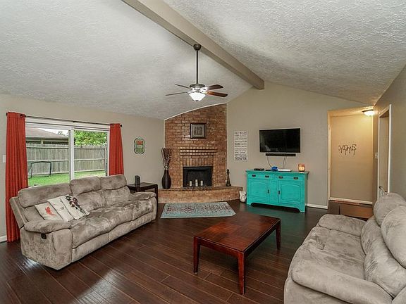 The family room has a corner fireplace with raised brick hearth, wood-look laminate flooring, ceiling fan, sliding door opening to the patio...