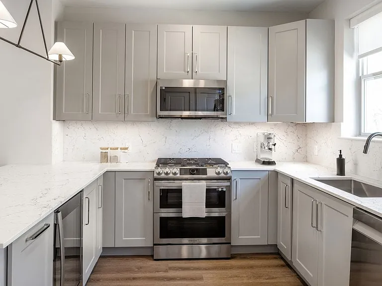 Signature Collection kitchen with stainless steel appliances, white quartz countertop, grey cabinetry, white quartz backsplash, and hard surface flooring