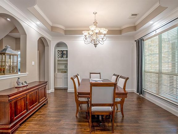 An elegant formal dining room features an intricate tray ceiling, gorgeous lighting, a wall of windows that allow for natural lighting and a neutral paint palette.