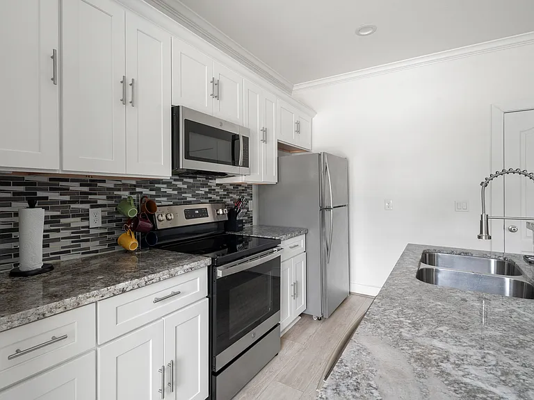 Stainless steel range and refrigerator in the fully furnished kitchen.