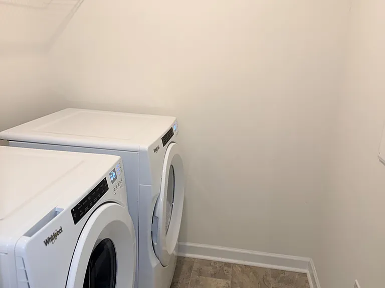 Dedicated laundry room with side-by-side front-load washer and dryer plus a wall shelf for supplies.
