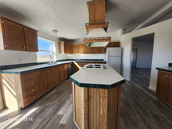 Kitchen, includes Oven/Store, Refrigerator, Dishwasher. Double sink has hand sprayer & soap dispenser. Counters: Corner counter (left &back), Island counter center, (includes stove), and counter on the right. Lots of cabinets and over the counter storage.