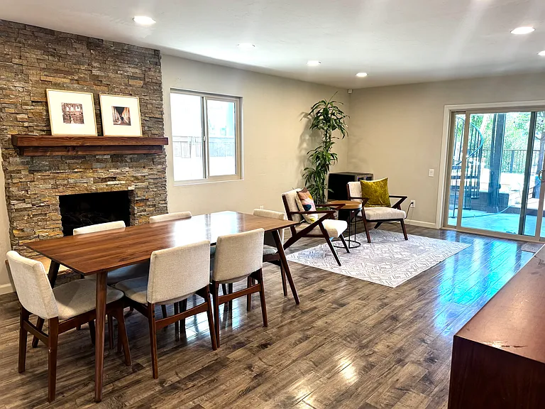Open-concept living and dining room with luxury vinyl plank flooring, recessed lighting, custom stacked-stone fireplace, and direct access to the spectacular backyard entertainment deck.