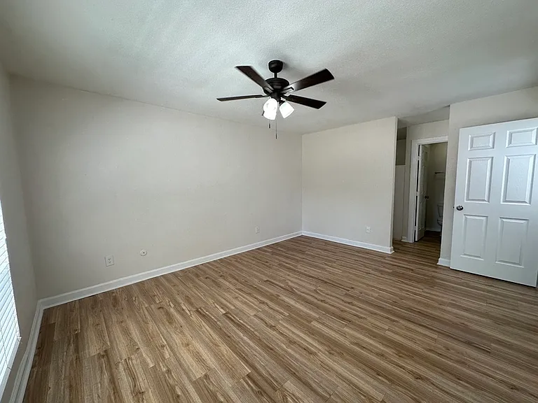 Spacious bedroom with elegant wood-style flooring, ceiling fan, and ample natural light. Spacious bedroom with elegant wood-style flooring, ceiling fan, and ample natural light.