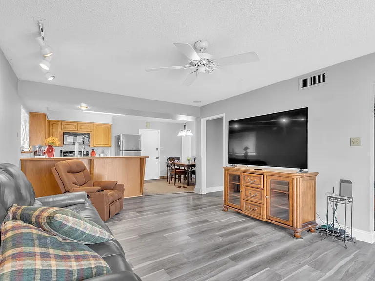 Living room with tv, couch that reclines and automatic recliner with heat and massage features. The kitchen and dining room table are in the back of the picture.