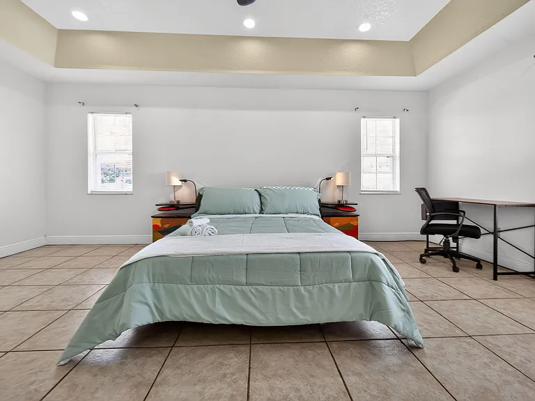 Spacious bedroom with a large bed setup, two windows, bedside tables, and a dedicated desk area for work or study.
