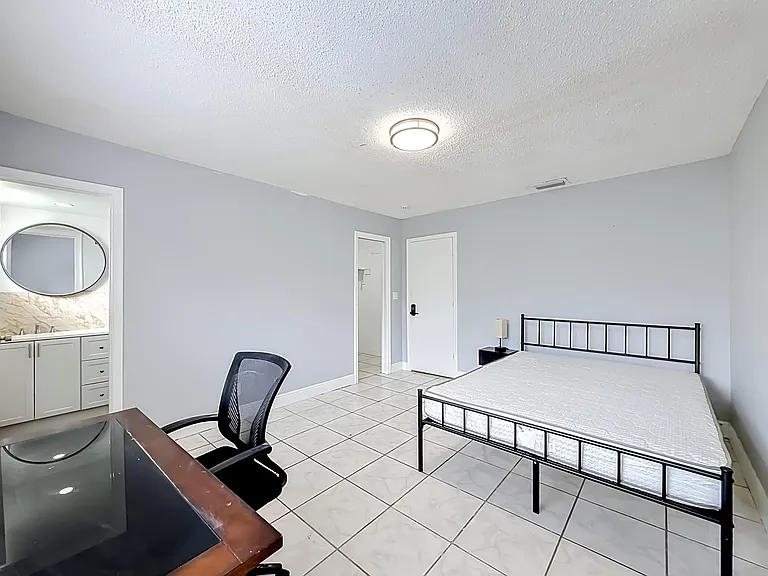 Spacious bedroom with tile flooring, a simple bed setup, and convenient access to a nearby vanity/sink area.
