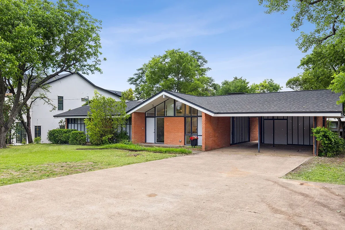 Mid-century modern exterior featuring a prominent carport, brick facade, and a striking A-frame entry with large glass panels - 6916 Forest Ln