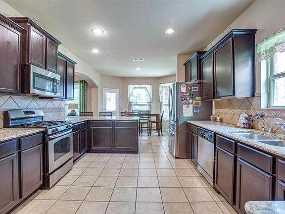 Spacious galley kitchen with ample dark cabinetry, granite counters, tile backsplash, and stainless appliances plus an eat-in