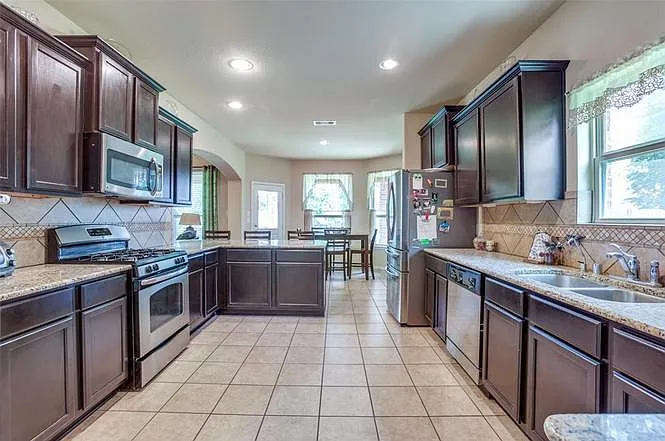 Spacious galley kitchen with ample dark cabinetry, granite counters, tile backsplash, and stainless appliances plus an eat-in