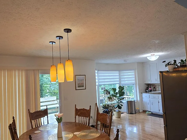 Dining area with a round table under pendant lighting, open to the kitchen and sliding doors leading to a deck.