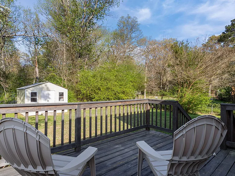 Elevated back deck with space for outdoor seating, overlooking a spacious, tree-lined yard and detached storage shed.