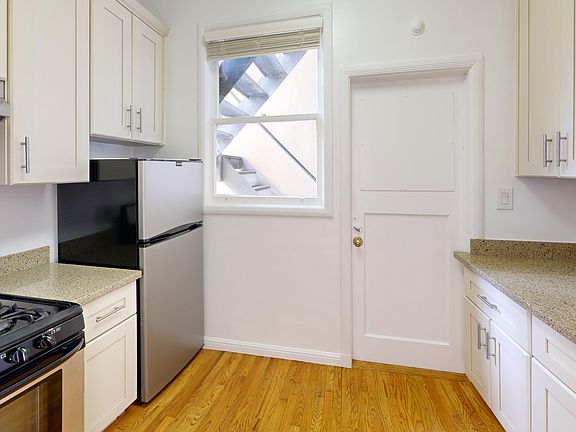 Bright kitchen with cabinets, granite countertops, and stainless steel appliances. Wood floor adds warmth. Window shows outdoor stairs.