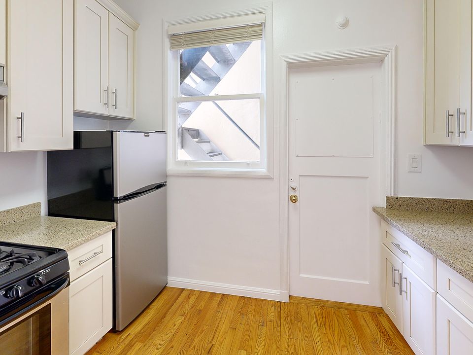 Bright kitchen with cabinets, granite countertops, and stainless steel appliances. Wood floor adds warmth. Window shows outdoor stairs.