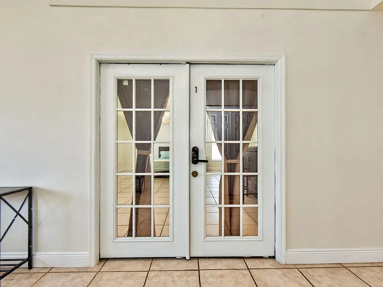 French doors with divided-light glass panels open to a tiled area and adjacent furnished room, adding flexible flow.