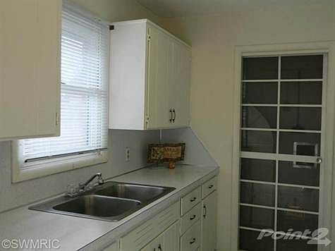 Bright white kitchen.  double sink.  Formica counters.  Utility/ mudroom door.  Garage access.