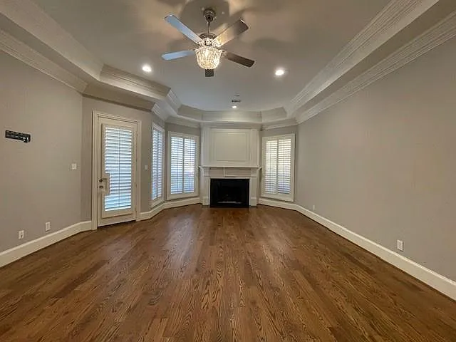 Unfurnished living room featuring a fireplace, dark wood-type flooring, ornamental molding, a tray ceiling, and a ceiling fan