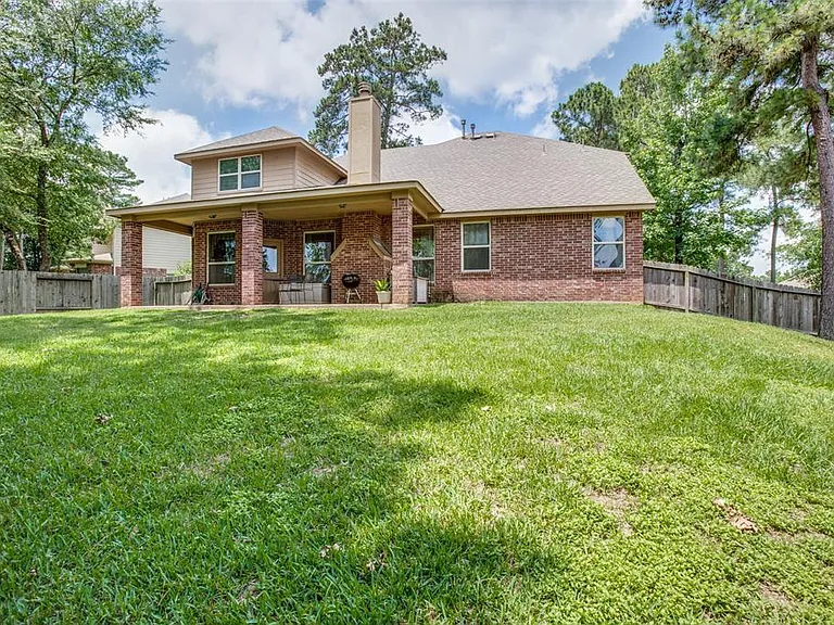 Fenced backyard with a covered patio and ample lawn space, ideal for outdoor dining, relaxing, or play.