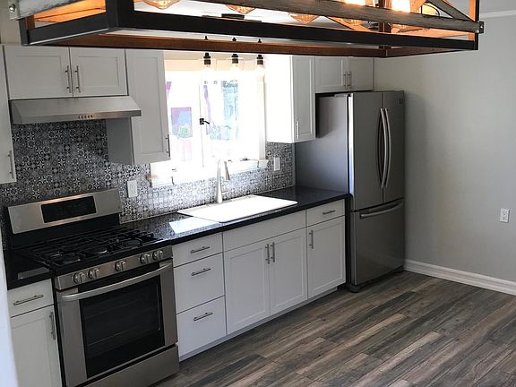 View of the spacious kitchen and dining area with fresh paint, new tile, fixtures, appliances, hardwood flooring, and cabinets.