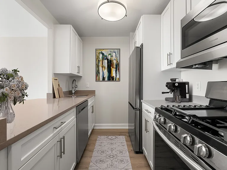 Sleek and modern kitchen with stainless steel appliances, stone countertops, six burner gas range, elegant white cabinetry, and stylish artwork, offering a perfect blend of functionality and design at Parkside Place, apartments in Cambridge, MA