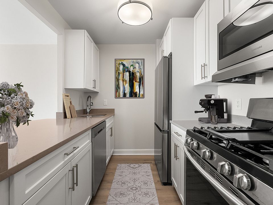 Sleek and modern kitchen with stainless steel appliances, stone countertops, six burner gas range, elegant white cabinetry, and stylish artwork, offering a perfect blend of functionality and design at Parkside Place, apartments in Cambridge, MA