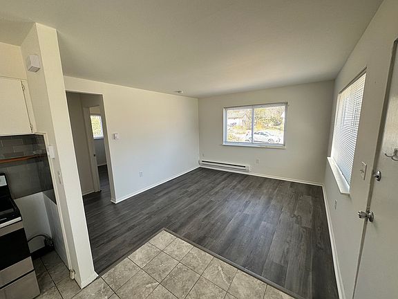 View of living room from kitchen with front door to the right. Large windows for lots of natural light.