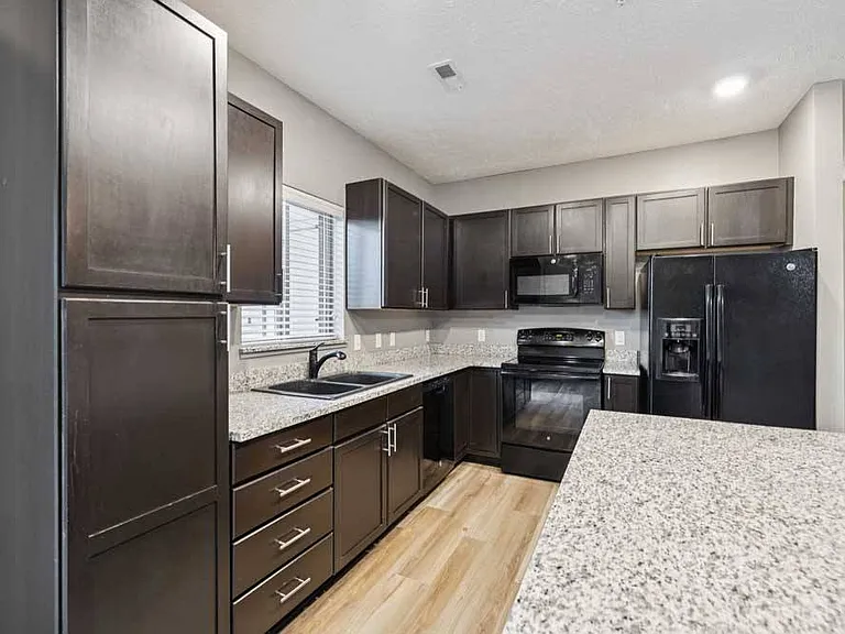 Cook and create with ease in this stylish kitchen featuring granite countertops, black appliances, and rich dark cabinetry with natural light from the window above the sink.