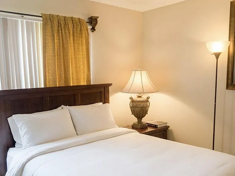 Comfortable bedroom featuring a full/queen bed, nightstand lighting, and a window with blinds and drapery for privacy.