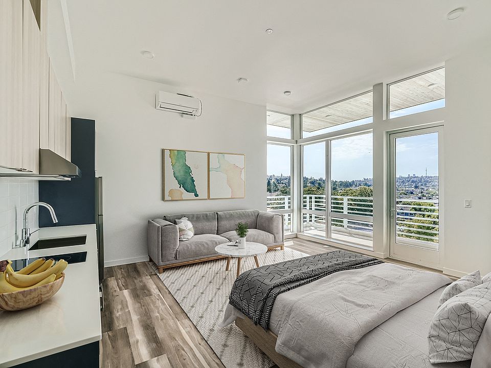 Relax in this inviting bedroom at Anker Ballard, featuring a comfortable bed, cozy couch, and large window that provides natural light and picturesque views.