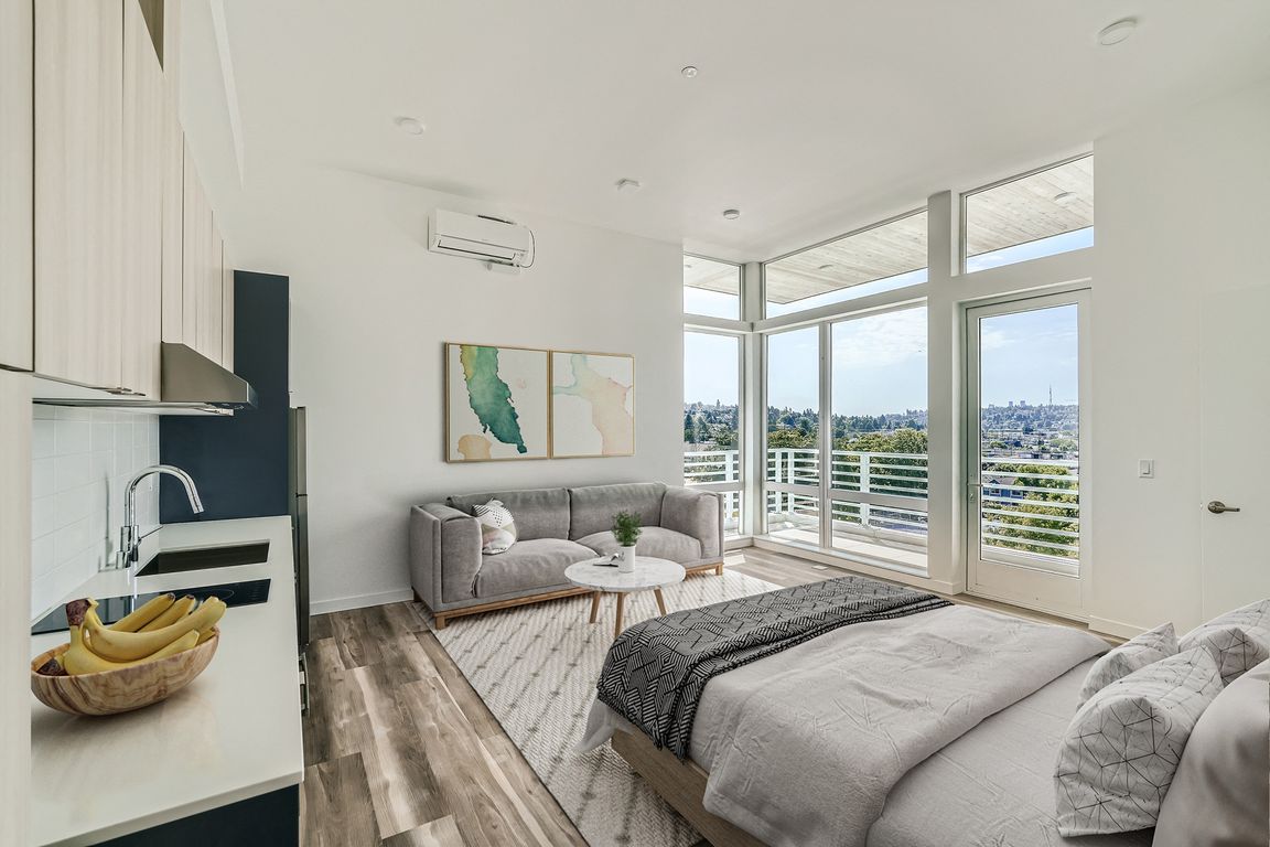 Relax in this inviting bedroom at Anker Ballard, featuring a comfortable bed, cozy couch, and large window that provides natural light and picturesque views.