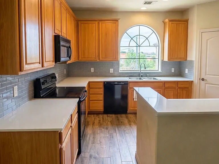 Open kitchen, large arched window overlooking front yard, granite countertops, tile backsplash, stainless appliances, breakfast bar, abundant natural light