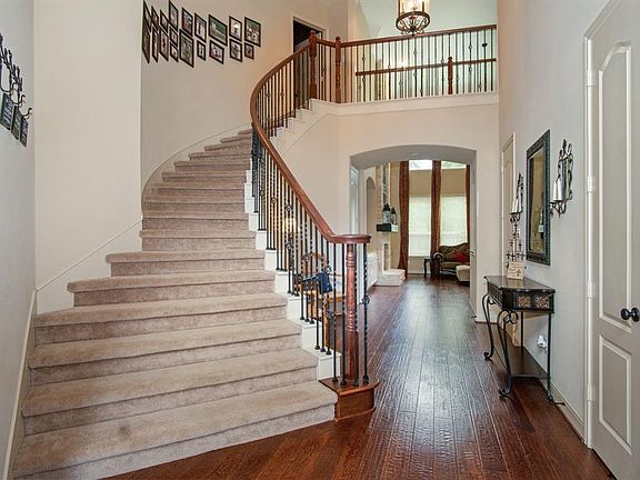 Elegant curved staircase with wrought iron spindles, hardwood floor, 2-story ceiling and lovely light fixture upon entry.