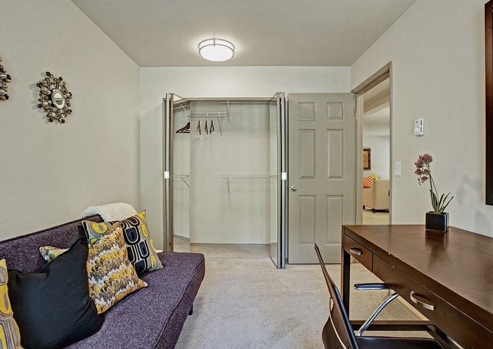 A bedroom used as a home office with a daybed, desk and chair, bookshelves, and a large window
