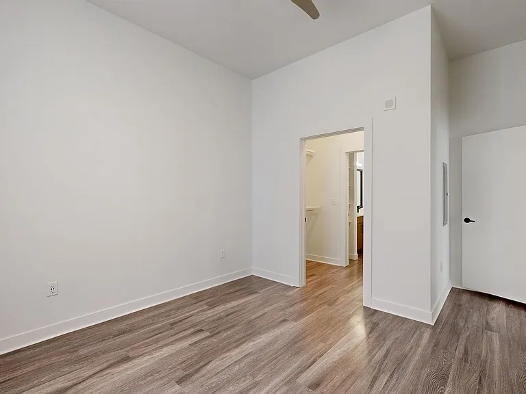 Spacious apartment bedroom with large closet, attached bathroom and wood-style flooring.
