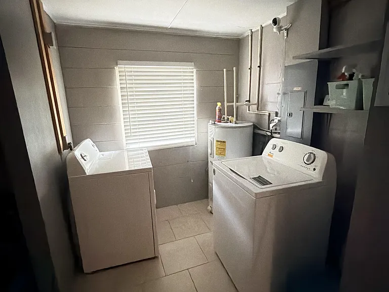 Dedicated laundry room with side-by-side washer and dryer, tiled flooring, shelving, and a window for ventilation.