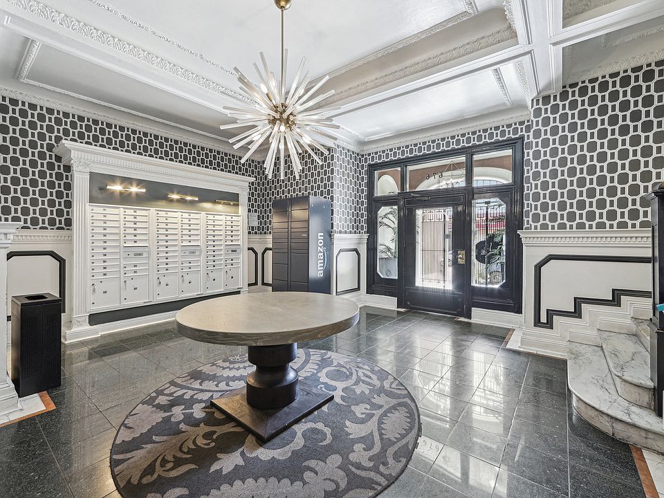 Lobby with geometric wallpaper, mailboxes, an Amazon locker, and a round table beneath a striking chandelier