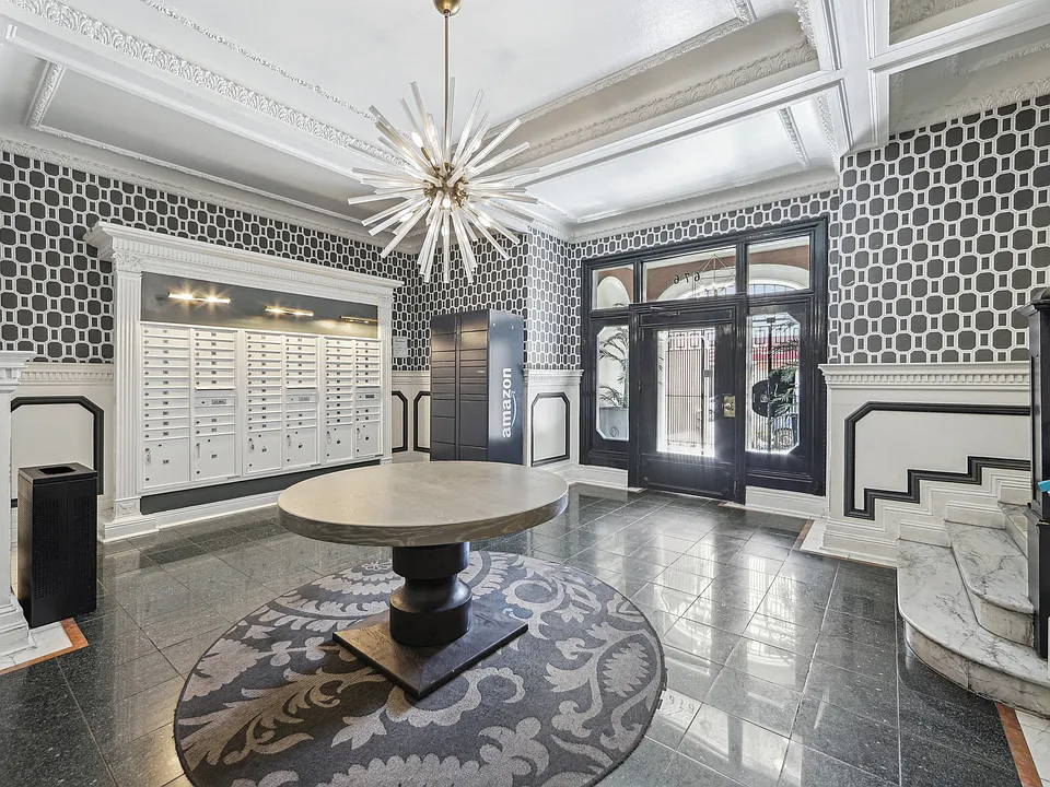 Lobby with geometric wallpaper, mailboxes, an Amazon locker, and a round table beneath a striking chandelier
