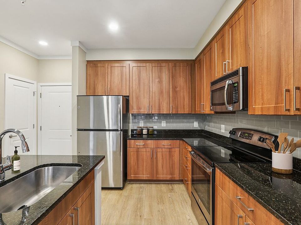 Renovated Package I kitchen with stainless steel appliances, oak cabinetry, grey tile backsplash, black granite countertops, and updated hard surface flooring and lighting