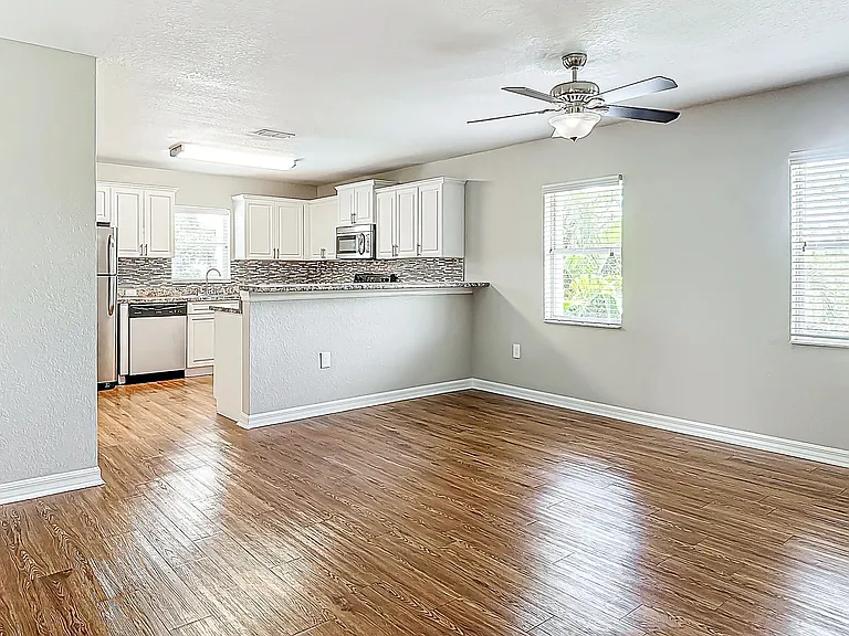 The open-concept design of this living area in The Suite floor plan seamlessly connects to a modern kitchen, featuring stainless steel appliances, hardwood floors, and ample natural light.
