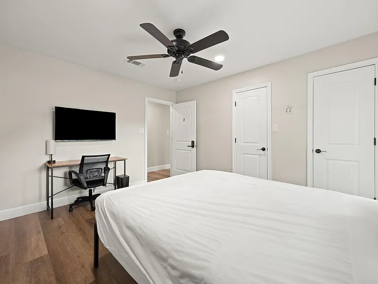 Private bedroom with hardwood-style floors, ceiling fan, wall-mounted TV, and a dedicated desk area for work or study.